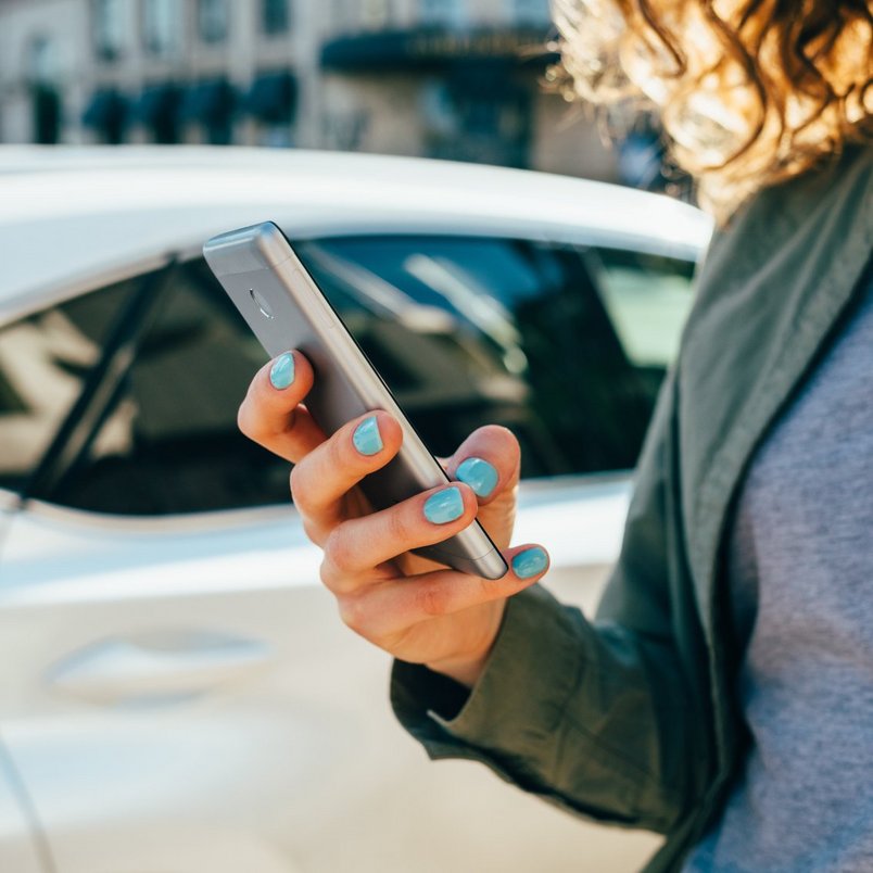 Frau mit Smartphone vor einem Auto