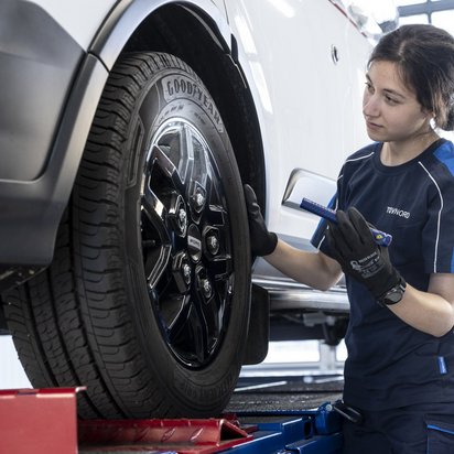 Auto auf Hebebühne und eine Frau steht mit einer Lampe am vorderen Reifen
