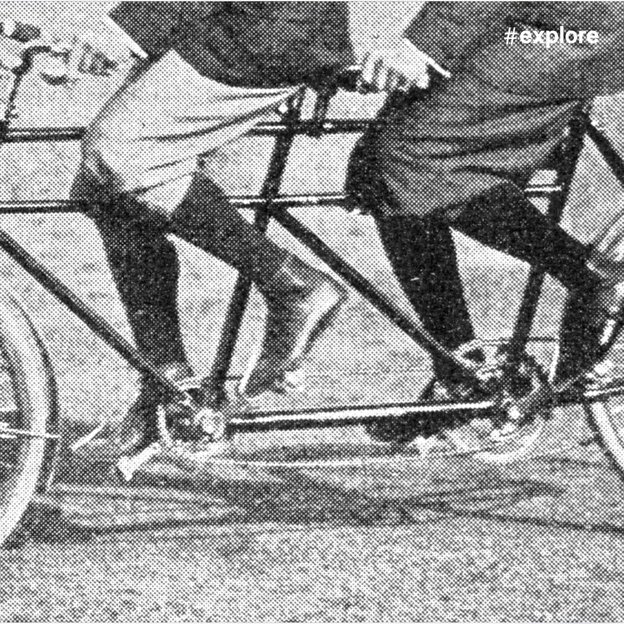 Schwarzweißfoto eines historischen Tandemfahrrads mit zwei Fahrern. Die komplexe Konstruktion zeigt die technische Innovation der Frühzeit des Radsports.