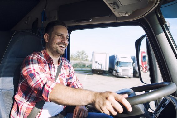 Lächelnder Lkw-Fahrer am Steuer auf einem Rastplatz bei Sonnenschein