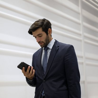 Geschäftsmann im Anzug blickt konzentriert auf sein Smartphone vor heller Wand