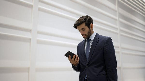 Geschäftsmann im Anzug blickt konzentriert auf sein Smartphone vor heller Wand