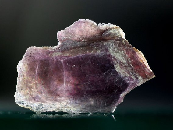 Großer, durchscheinender Kristall in violetten und rosa Tönen mit glatten, facettierten Oberflächen und weißlichen Rändern.