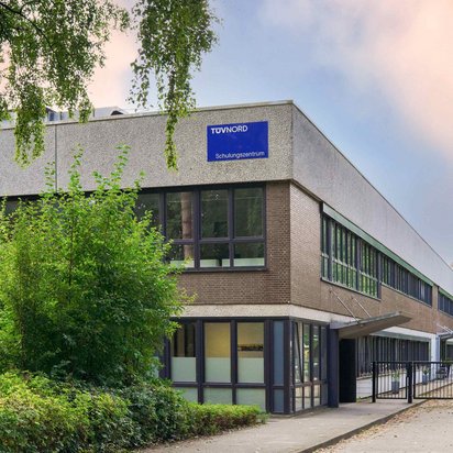Außenansicht des TÜV NORD Schulungszentrums in Hamburg, ein modernes Gebäude mit großen Fenstern und einem blauen Schild.