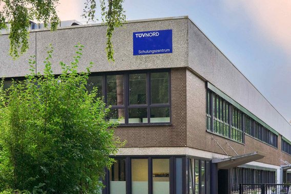 Außenansicht des TÜV NORD Schulungszentrums in Hamburg, ein modernes Gebäude mit großen Fenstern und einem blauen Schild.