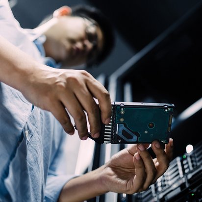 Eine Person setzt eine Festplatte in ein Serverrack ein und führt technische Arbeiten an der Hardware durch.