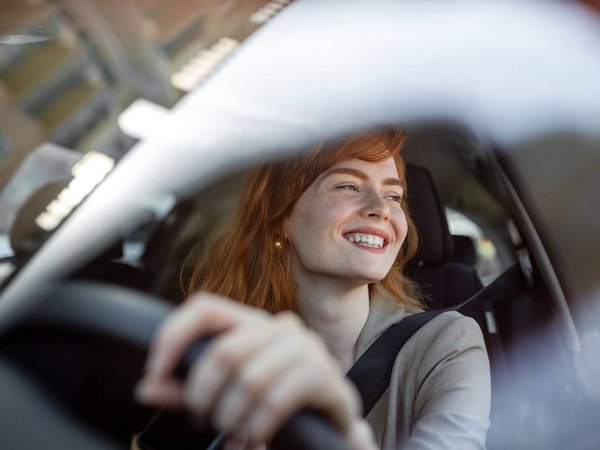 Lächelnde Frau am Steuer eines Autos, aufgenommen durch die Windschutzscheibe