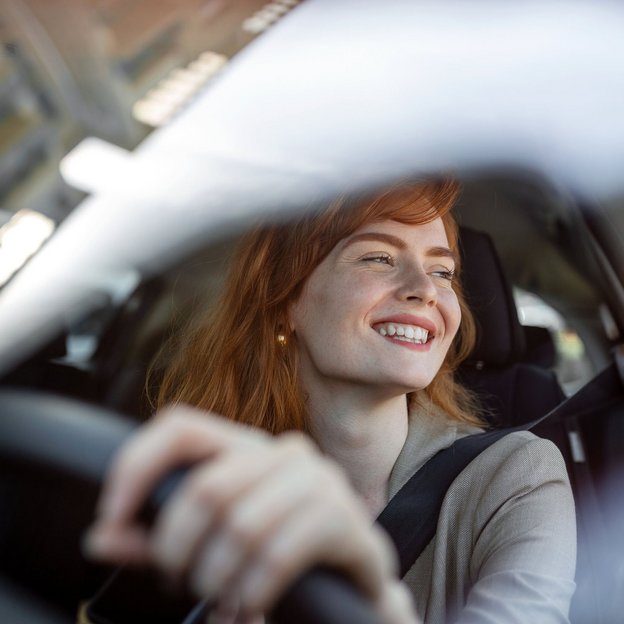Lächelnde Frau am Steuer eines Autos, aufgenommen durch die Windschutzscheibe