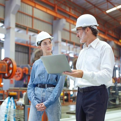 Arbeitsschutzmanagement-Auditor (TÜV) Zwei Personen mit Schutzkleidung stehen in einer Lagerhalle und reden miteinander.