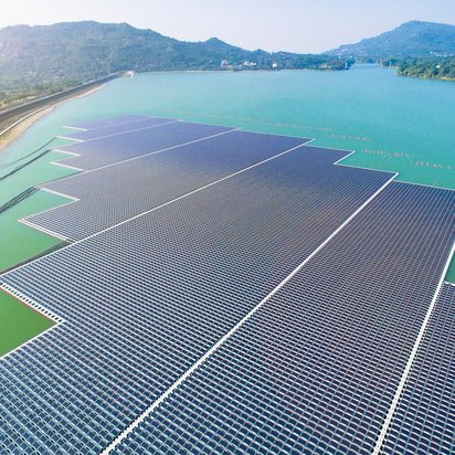 Große schwimmende Solaranlage auf einem türkisfarbenen See. Die rechteckige Anlage besteht aus tausenden Solarmodulen und ist von Bergen umgeben.