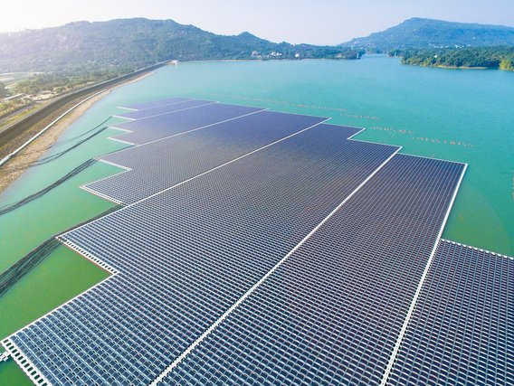 Große schwimmende Solaranlage auf einem türkisfarbenen See. Die rechteckige Anlage besteht aus tausenden Solarmodulen und ist von Bergen umgeben.