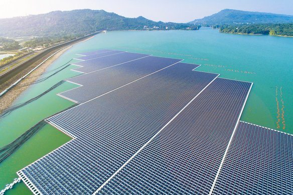 Große schwimmende Solaranlage auf einem türkisfarbenen See. Die rechteckige Anlage besteht aus tausenden Solarmodulen und ist von Bergen umgeben.