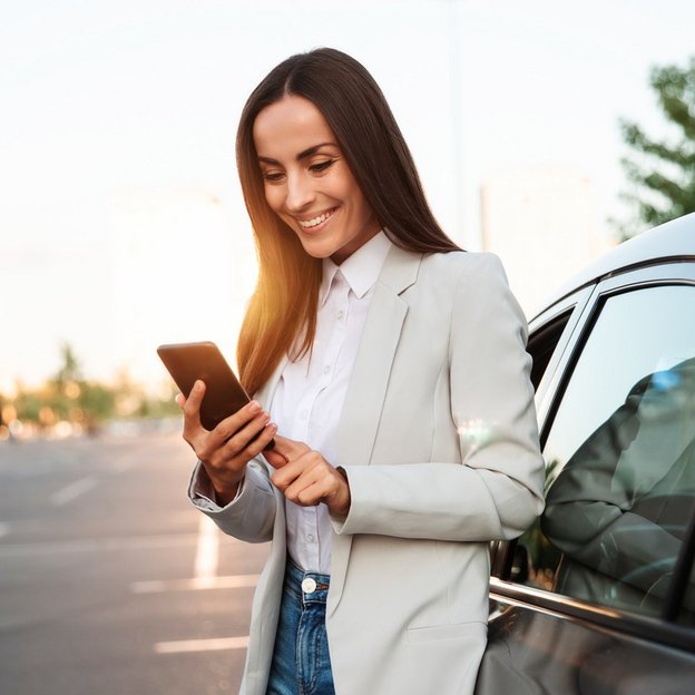 Frau steht neben einem Auto und benutzt ein Smartphone