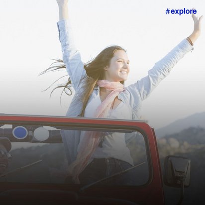 Junge Frau mit rosa Schal jubelt mit erhobenen Armen durch das Schiebedach eines roten Autos in bergiger Landschaft.