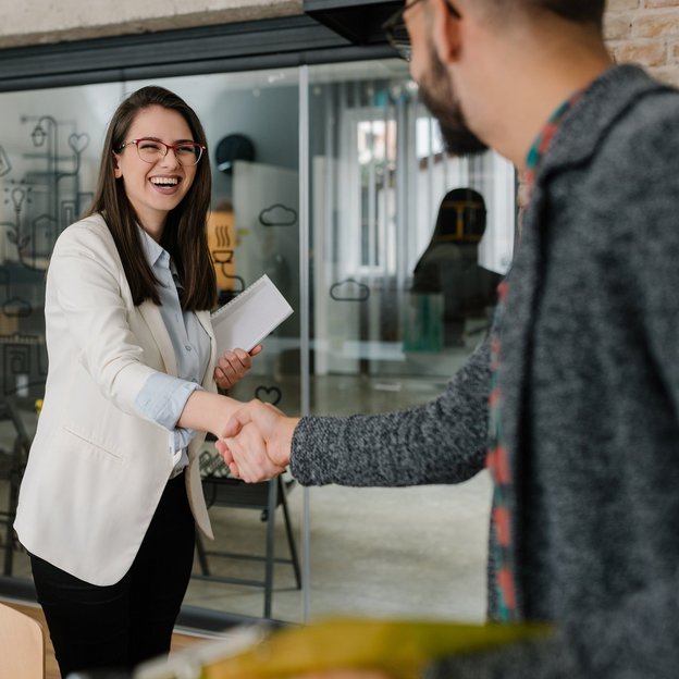 Zwei Personen begrüßen sich per Handschlag in einem modernen Büro.