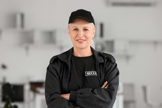 Sicherheitskraft in schwarzer Uniform mit verschränkten Armen, ausgestattet mit Handschellen und Funkgerät, symbolisiert professionelle Sicherheit und Schutz.