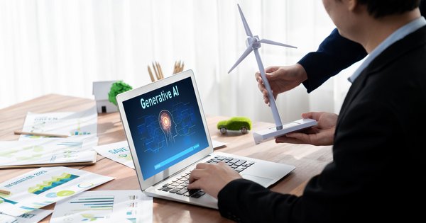 Person zeigt ein Modell-Windrad neben einem Laptop mit „Generative AI“-Anzeige auf dem Bildschirm.