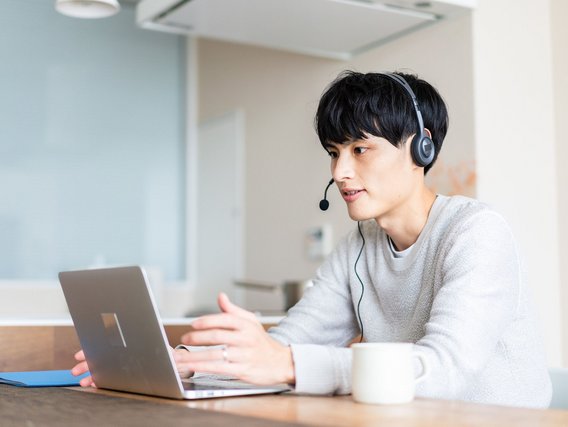 Junger Mann mit Headset nimmt an einem Online-Meeting über Laptop teil.