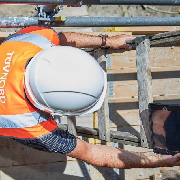 Experte mit Helm und Warnweste bei einer technischen Prüfung auf einer Baustelle im Rahmen der Bausanierung.