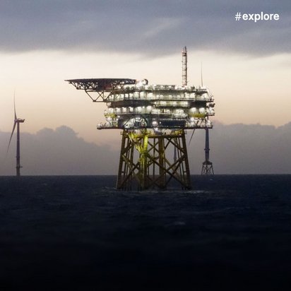 Atmosphärische Aufnahme einer Offshore-Plattform und mehrerer Windkraftanlagen im Meer bei Dämmerungslicht, die gemeinsam eine nachhaltige Energieproduktion auf See darstellen.