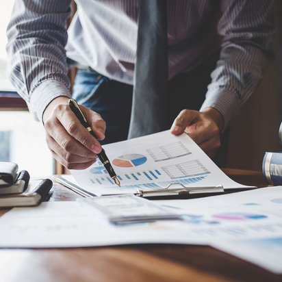 Finanzanalyse und Dokumentenprüfung im Büro Geschäftsmann analysiert Finanzdiagramme auf Schreibtisch mit Dokumenten und Büchern.