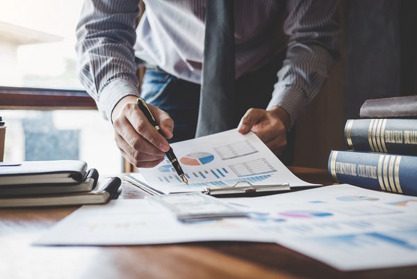 Geschäftsmann analysiert Finanzdiagramme auf Schreibtisch mit Dokumenten und Büchern.