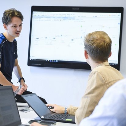 3 Personen stehen vor einem Bildschirm und unterhalten sich