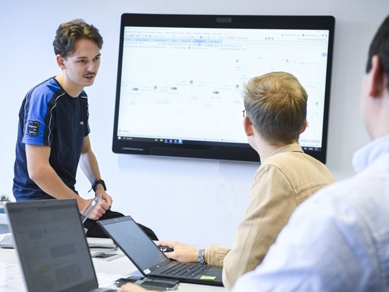 3 Personen stehen vor einem Bildschirm und unterhalten sich