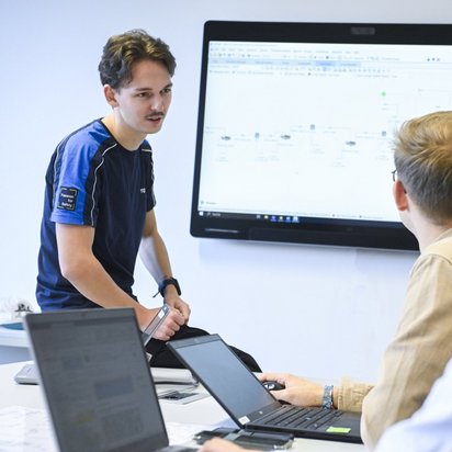 3 Personen stehen vor einem Bildschirm und unterhalten sich