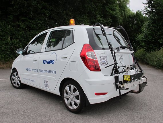 Weißer TÜV NORD Messfahrzeug mit Abgasmessgerät am Heck und orangem Warnlicht für mobile Emissionsprüfungen.