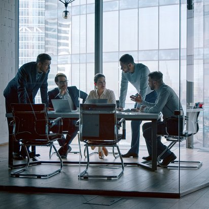 Fünf Personen diskutieren konzentriert in einem modernen, verglasten Konferenzraum