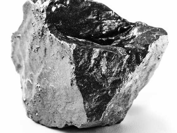 Ein grauweißer Gesteinsbrocken mit großen, schwarzen, glänzenden Mineraleinschlüssen, die eine spiegelnde Oberfläche aufweisen.