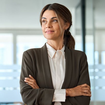 Eine Datenschutzbeauftragter steht im Büro mit verschränkten Armen und trägt ein Business‑Outfit.