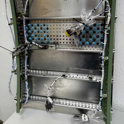 Ein Metallrahmen mit Kabeln und elektronischen Komponenten, die sorgfältig angeordnet sind. Die Szene zeigt die Komplexität der Flugzeugelektrik in der Luftfahrttechnik.