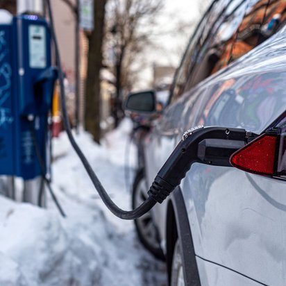 Weißes Auto steht bei Schnee an einer Ladestation und lädt