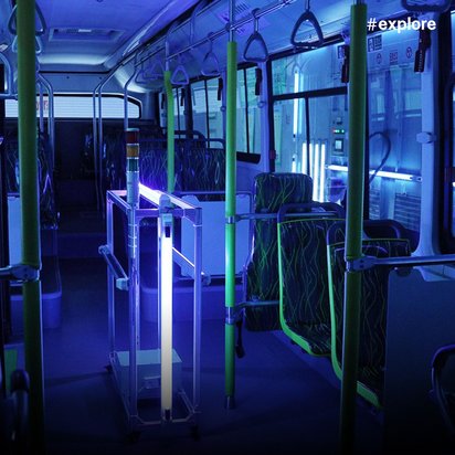Das Innere eines leeren Busses, das mit blauem UV-Licht zur Desinfektion beleuchtet ist, zeigt Sitze, Haltestangen und mehrere UV-Lampen an der Decke.