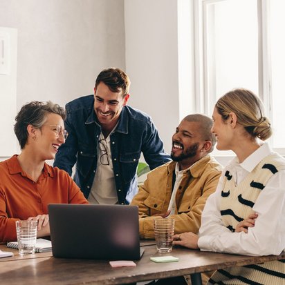 Konstruktiver Austausch im Projektteam während eines Meetings. Vier Kolleg:innen sitzen gemeinsam an einem Tisch und besprechen Inhalte auf einem Laptop.