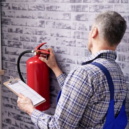  Techniker prüft Feuerlöscher an der Wand und dokumentiert die Ergebnisse auf einem Klemmbrett.