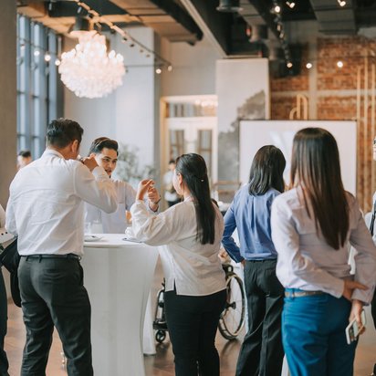 Menschen in Businesskleidung stehen bei einer Tagung an Stehtischen und unterhalten sich