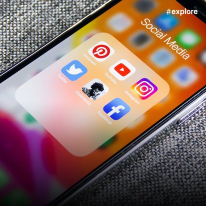 Ein Smartphone auf grauem Stoffuntergrund zeigt einen Ordner mit Social-Media-Apps wie Pinterest, Twitter, YouTube, Instagram und Facebook.