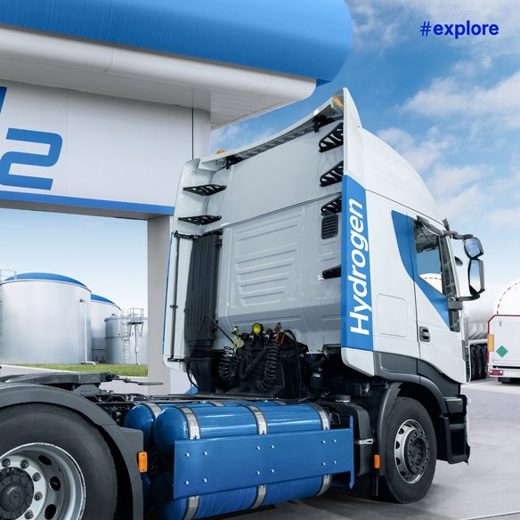 Ein moderner Wasserstoff-LKW steht an einer Wasserstofftankstelle. Der LKW ist mit großen Wasserstofftanks ausgestattet. Im Hintergrund sind weitere Tanks und ein klarer blauer Himmel zu sehen.