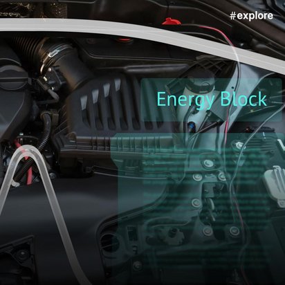 Ein durchsichtiges Augmented-Reality-Display zeigt die digitale Überlagerung eines Automotors mit türkisfarbenen Hervorhebungen und der Beschriftung "Energy Block" im Fahrzeuginnenraum.