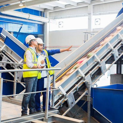 Zwei Personen besichtigen eine Recyclinganlage zur Abfallwirtschaft