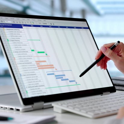 Hand zeigt mit Stift auf Gantt-Diagramm auf einem Laptop zur Projektplanung und Aufgabenverfolgung