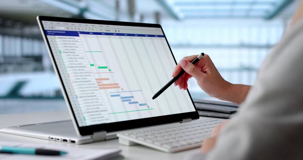 Hand zeigt mit Stift auf Gantt-Diagramm auf einem Laptop zur Projektplanung und Aufgabenverfolgung