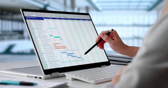 Hand zeigt mit Stift auf Gantt-Diagramm auf einem Laptop zur Projektplanung und Aufgabenverfolgung