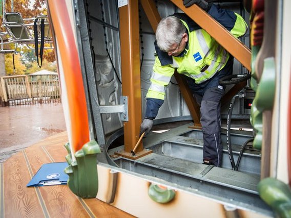Ein Wartungstechniker in gelber Sicherheitsweste arbeitet im Inneren eines Karussells, beugt sich vor, um mit einem Werkzeug etwas zu reparieren.