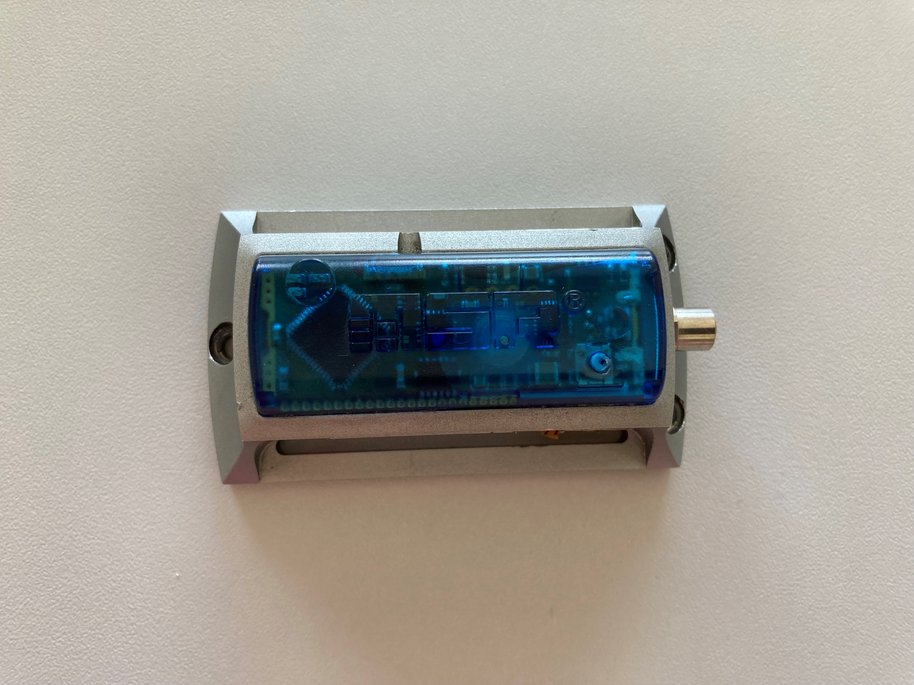 Elektronisches Gerät mit transparentem blauen Gehäuse und silberner Umrandung an weißer Wand montiert.