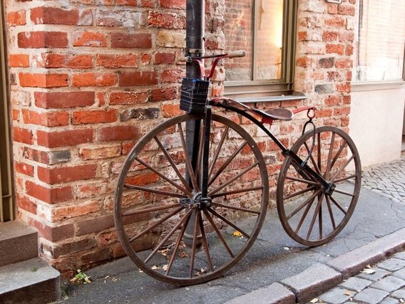 Ein altertümliches Fahrrad mit großen Holzspeichenrädern, angelehnt an eine Backsteinmauer. Ein historisches Zweirad aus der Anfangszeit der Fahrradentwicklung.