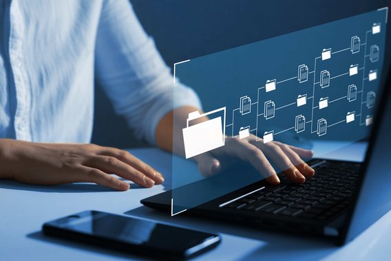 Person tippt auf Laptop mit schwebendem Interface aus Ordner- und Dokumentensymbolen.